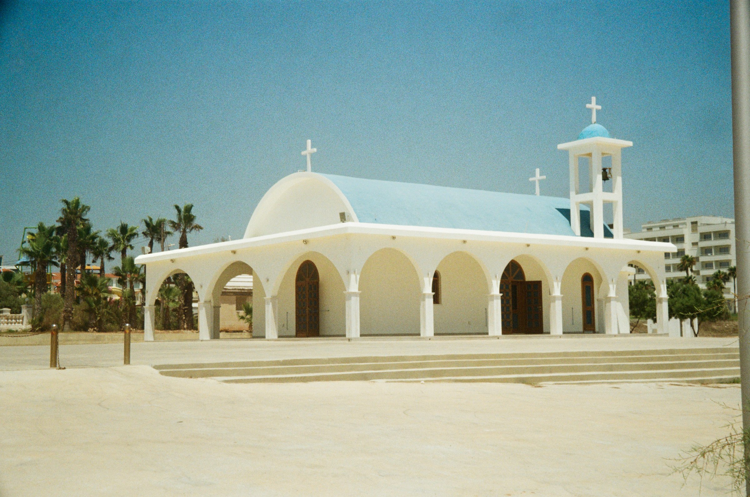 A whitewashed chapel with a blue dome, palm trees alongside
