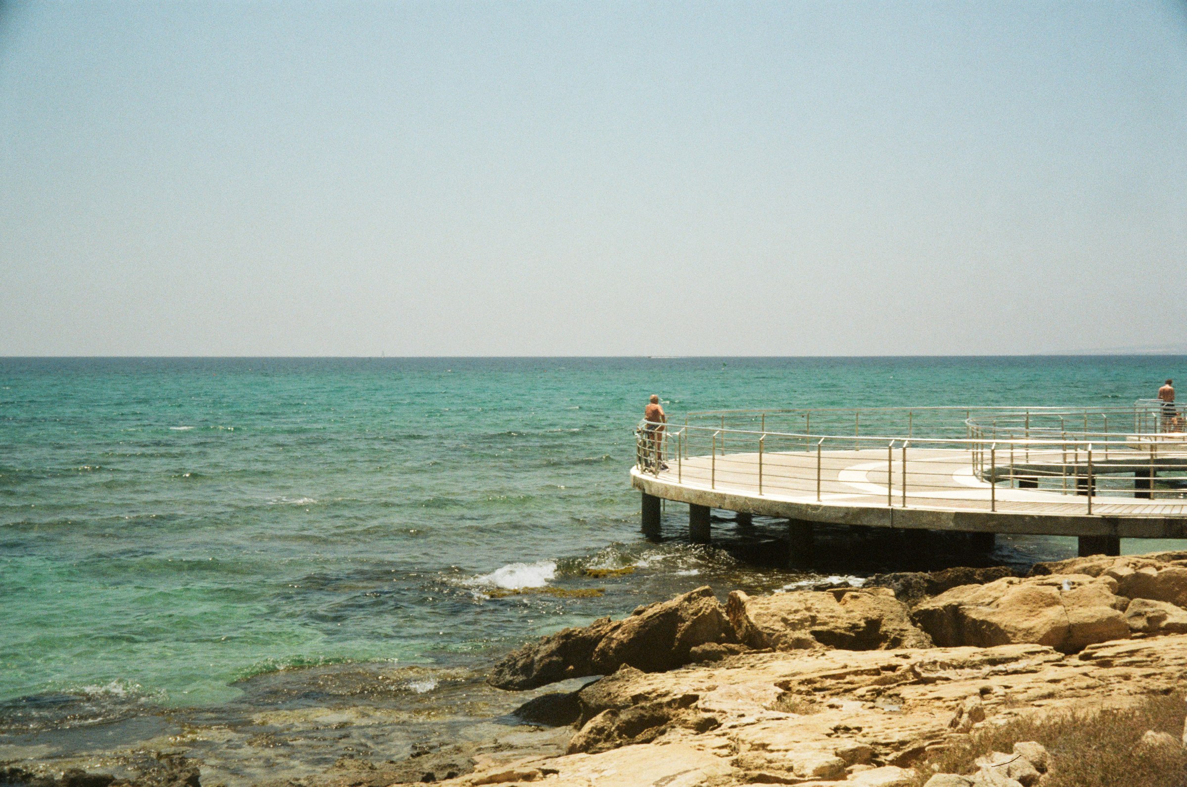 A pier over turquoise water along a rocky coast